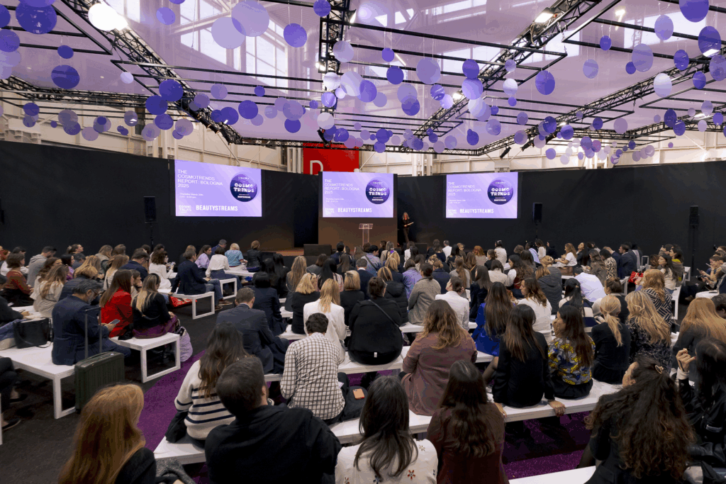 Attendees listening to a speaker at a Cosmoprof beauty trade show
